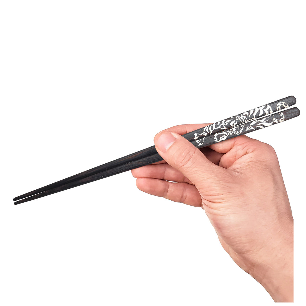 Black chopsticks with tiger engraving being held by a hand full image. Not personalized